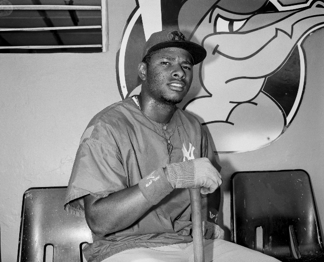 Black and white photo of a baseball player seated holding a bat. 